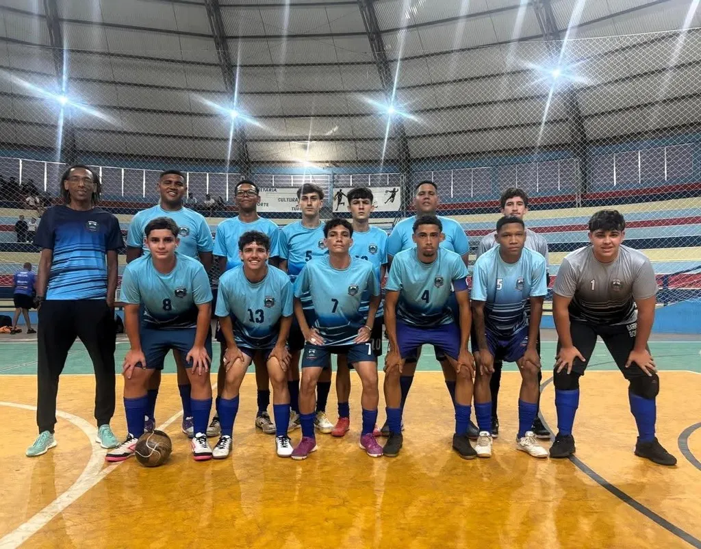 equipe de jogadores com uniforme em tom de azulm numa quadra de piso amarelo e bem iluminada