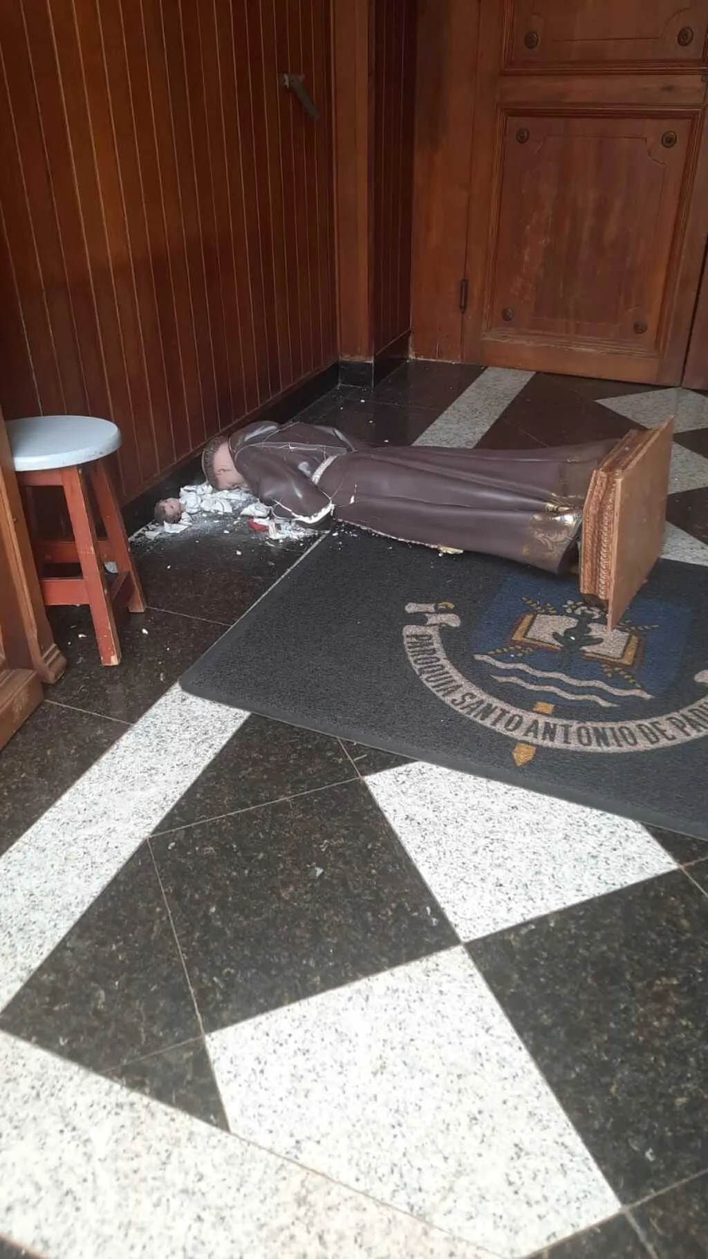 Imagem de Santo Antonio quebrada, com um banco ao lado e chão na cores preta e branca