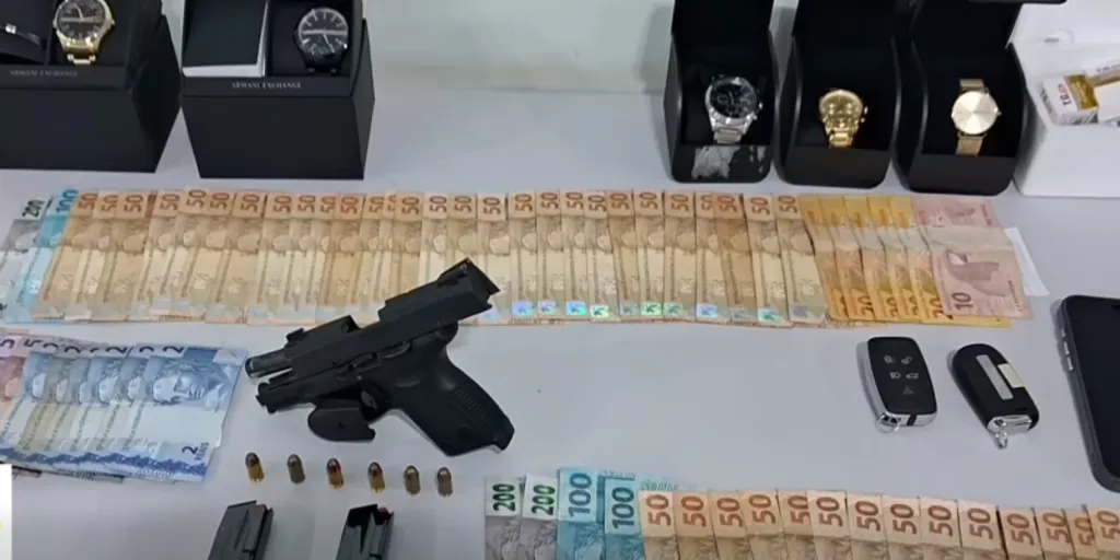 bancada com dinheiro, relógios, arma e chaves de carro expostos pela polícia civil