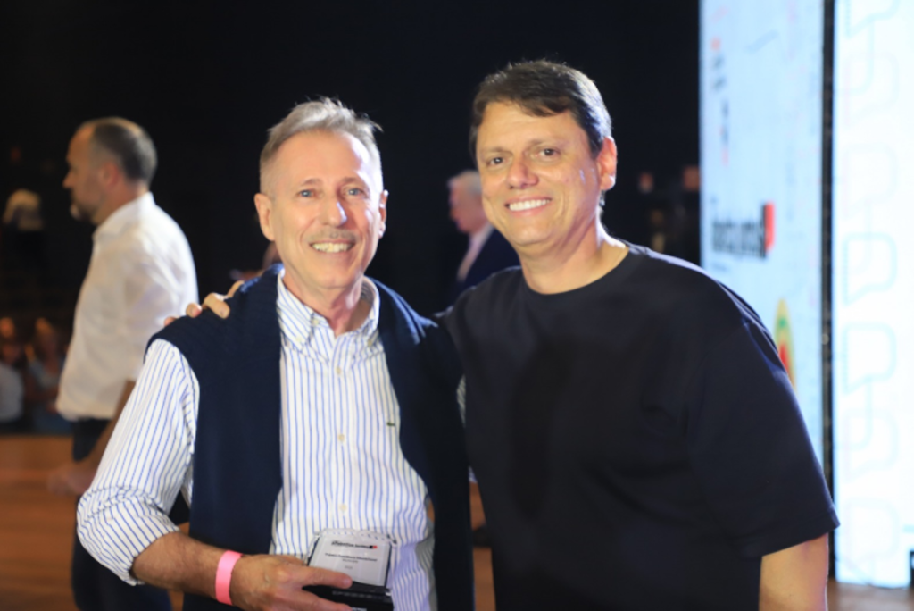 homem de camisa social segura troféu ao lado de outro, com camiseta preta