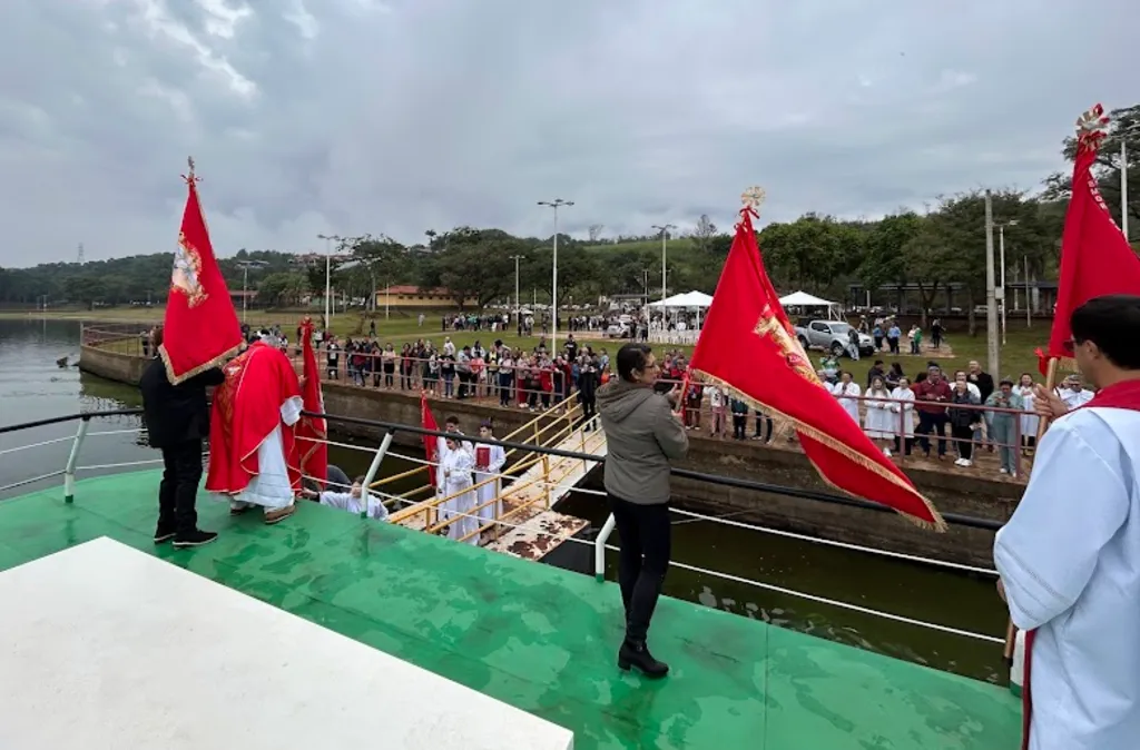pessoas num barco de chão verde acenam com bandeiras vermelhas para quem está namargem de um cais