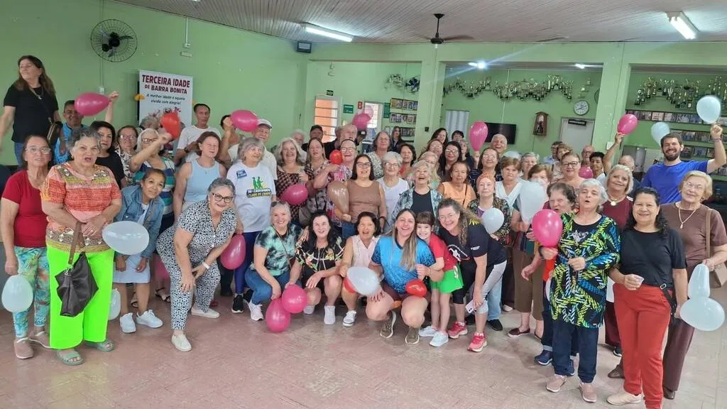 grande grupo de pessoas, idosas, posa para foto em local arejado com fundo verde