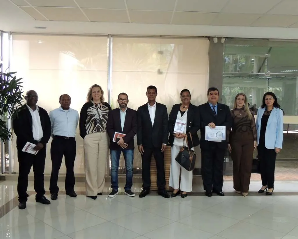 Nove pessoas vestidas formalmente posam lado a lado no saguão do evento, com uma delas segurando um certificado.