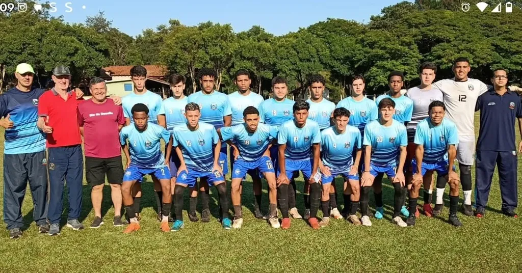 foto de toda a equipe de futebol com uniforme em tom de azul e comissão técnica ao lado num gramado