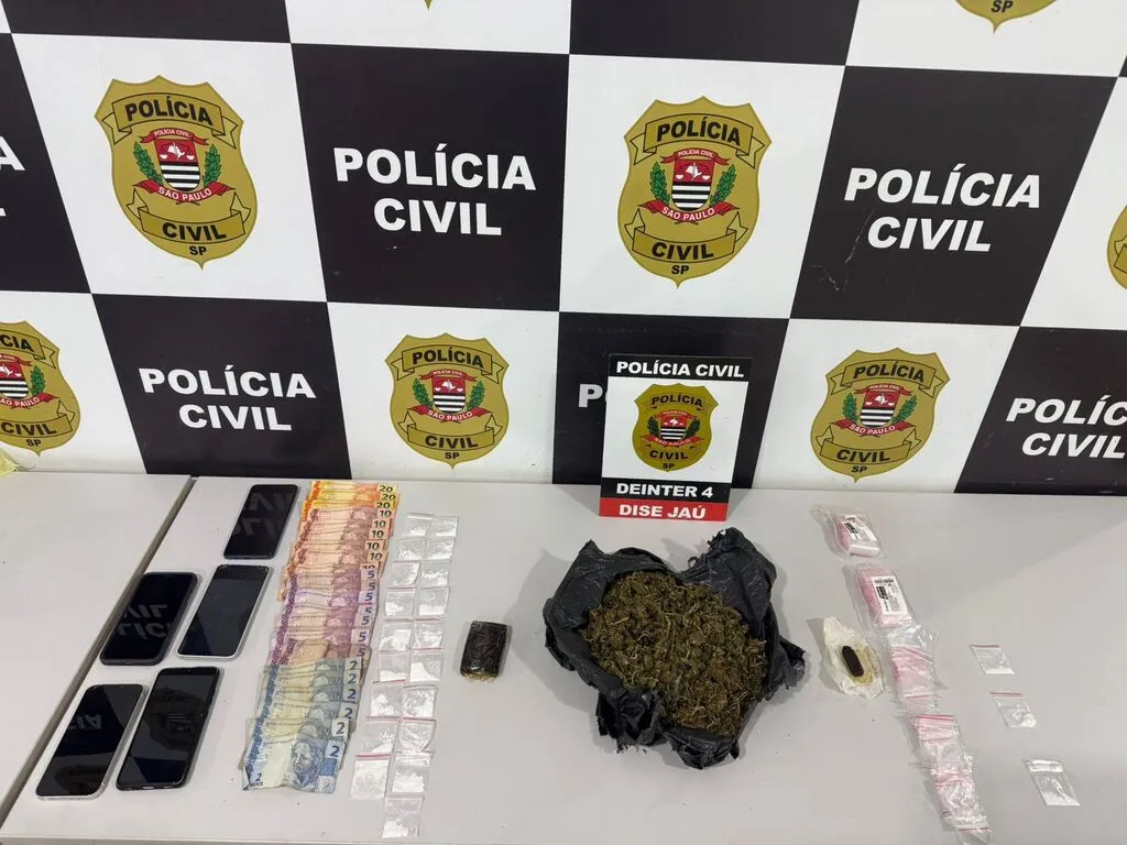 Mesa branca contendo diversos telefones celulares, dinheiro em notas diversas e maconha em saco plástico preto, além de embalagens transparentes