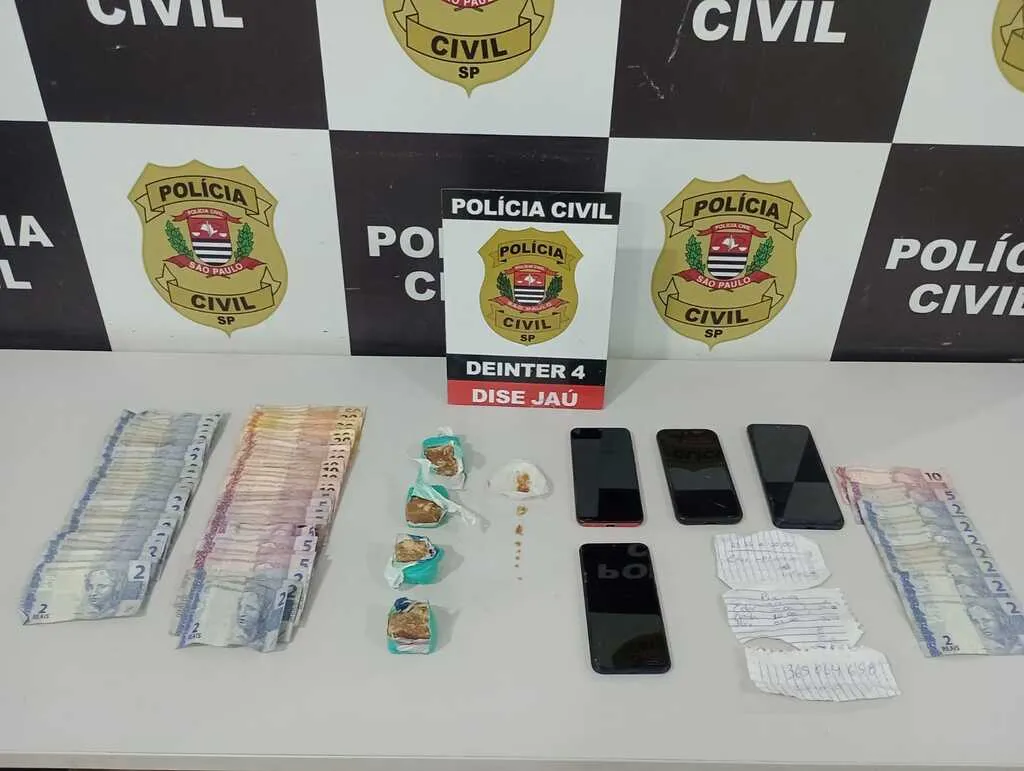 Mesa contendo dinheiro, telefones celulares, papéis e pedras de crack com um painel com os dizeres Polícia Civil ao fundo