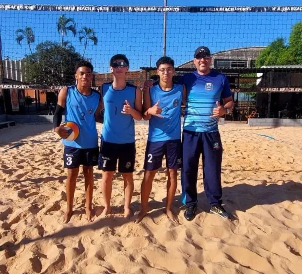 trÊs jovens e um homem de azul num espaço com areio no chão e uma rede ao fundo