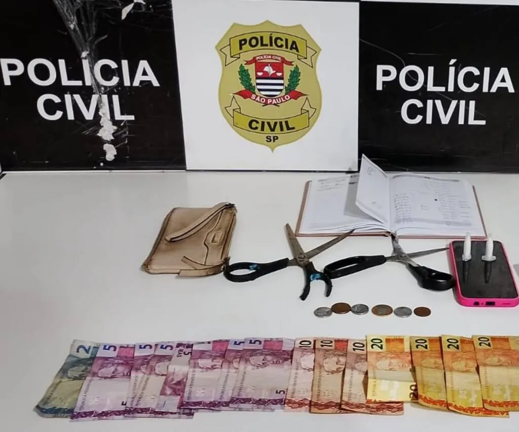 Painel da Polícia Civil tendo a frente duas tesouras, agenda, telefone celular e dinheiro em cédulas e moedas