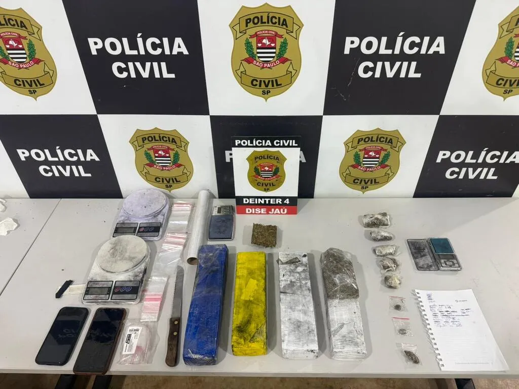 Mesa com celulares, balanças e materiais diversos, além de um painel ao fundo com escrito Polícia Civil