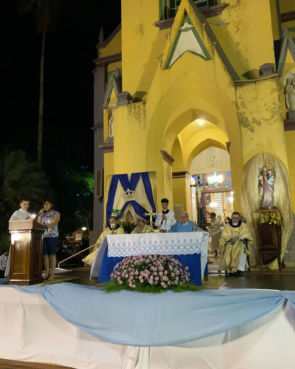 Altar montado em frente a um templo da igreja católica, com toalha azul e branca e um crucifixo em cima
