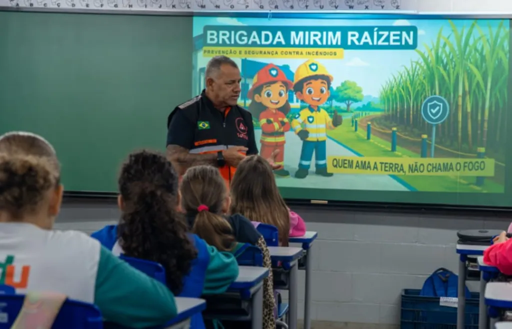 homem de uniforme de bombeiros fala em sala de aula com crianças e lousa verde ao fundo